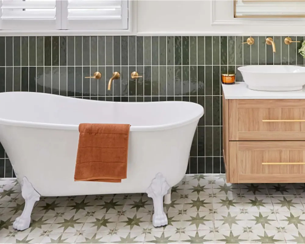 Modern bathroom with white clawfoot tub, orange towel, green tile backsplash, wooden vanity, and star-patterned floor tiles.
