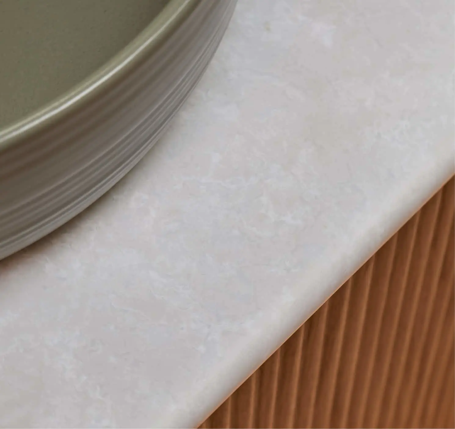 Close up of the edge of a sage basin on a white vanity countertop.