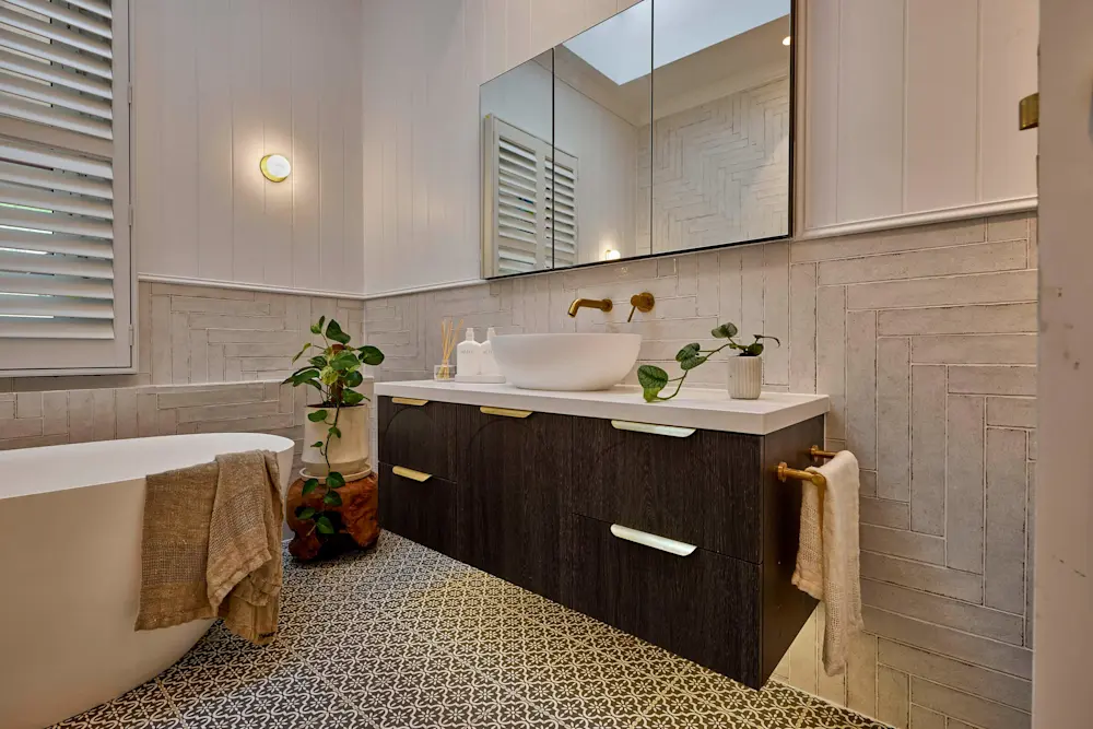 Modern bathroom with white vessel sink, dark wood vanity, patterned floor tiles, white bathtub, and green plants.