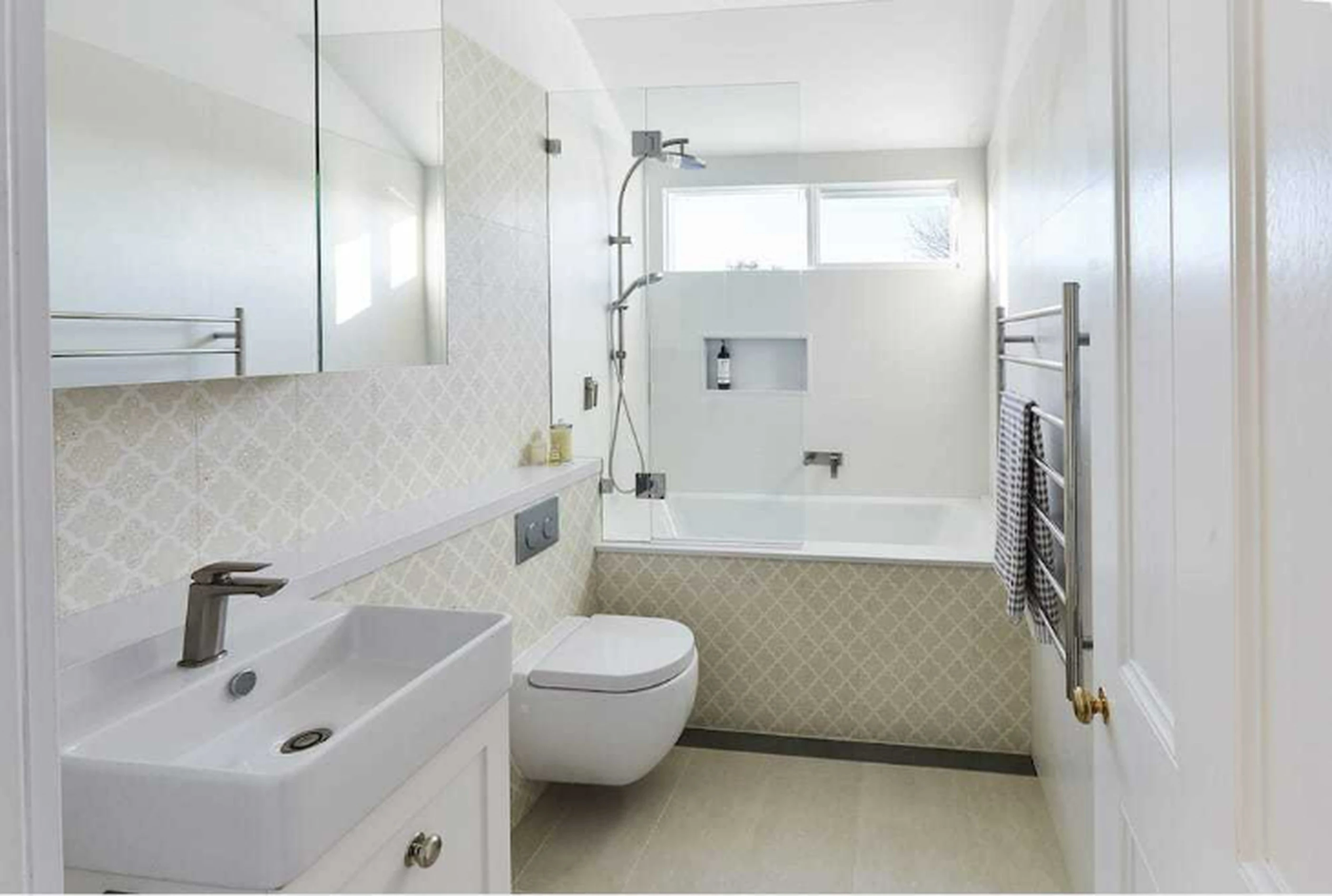 Modern white bathroom with patterned tile, glass shower enclosure, wall-mounted toilet, and heated towel rail.