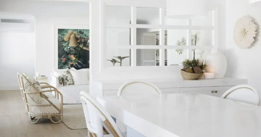 Bright white living space with rattan chairs, white dining table, window partition, and tropical decor with pineapples.