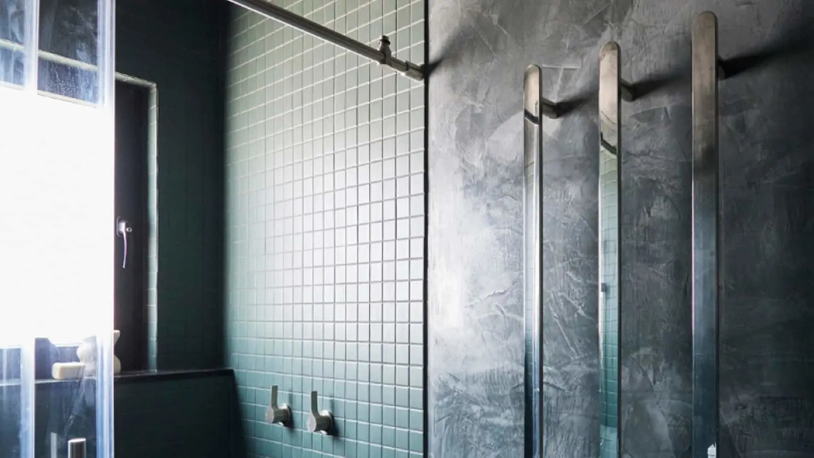 Modern bathroom with mint green tile walls, concrete textured wall, and glass shower enclosure.