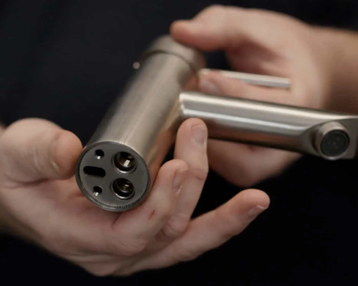 Hands holding a brushed nickel tap, so that you can see the bottom and the connections available.