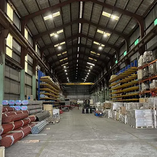 Interior of a large warehouse with high ceilings, stacked materials, and organised shelving for industrial supplies.