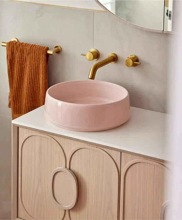 Modern bathroom with pink vessel sink, brass fixtures, wooden vanity, and orange towel on gold towel bar.