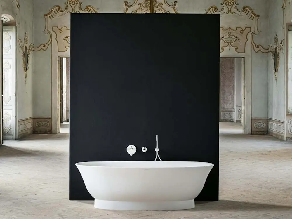 Modern white bathtub against black panel in ornate historic room with decorative walls and doorways.
