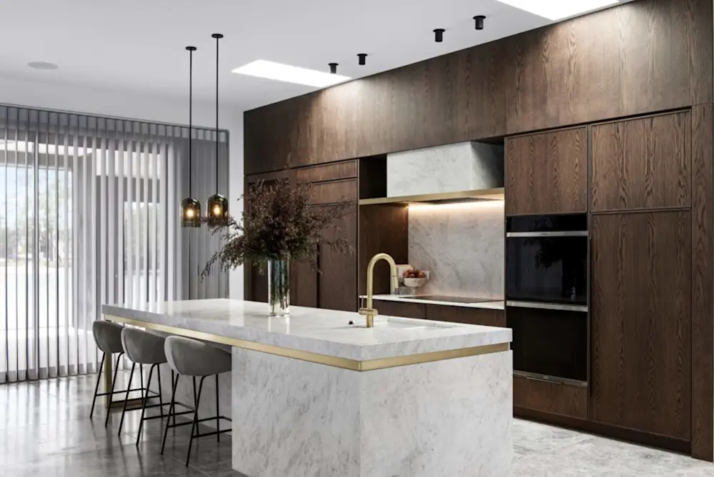 Modern kitchen with marble island, dark wood cabinets, gold fixtures, pendant lights, and gray bar stools.