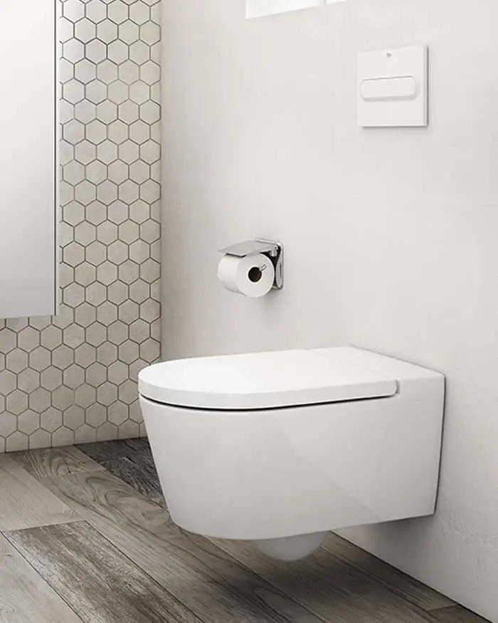 Modern white wall-mounted toilet with hexagonal tile accent wall, wooden floor, and chrome toilet paper holder.