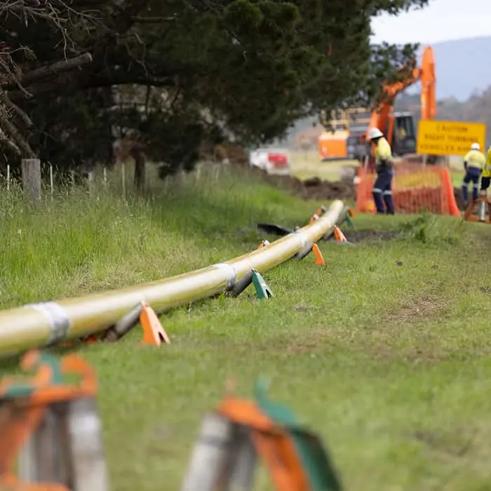 Yellow pipeline being installed in grassy field with construction workers and orange excavator in background.
