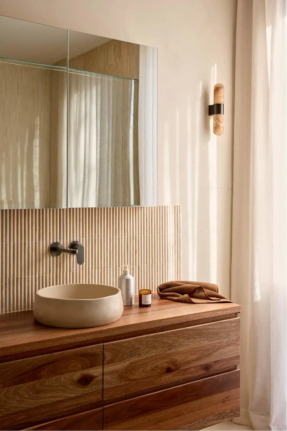 Bathroom with round white sink on wooden vanity, mirror above textured wall, and wall-mounted faucet.