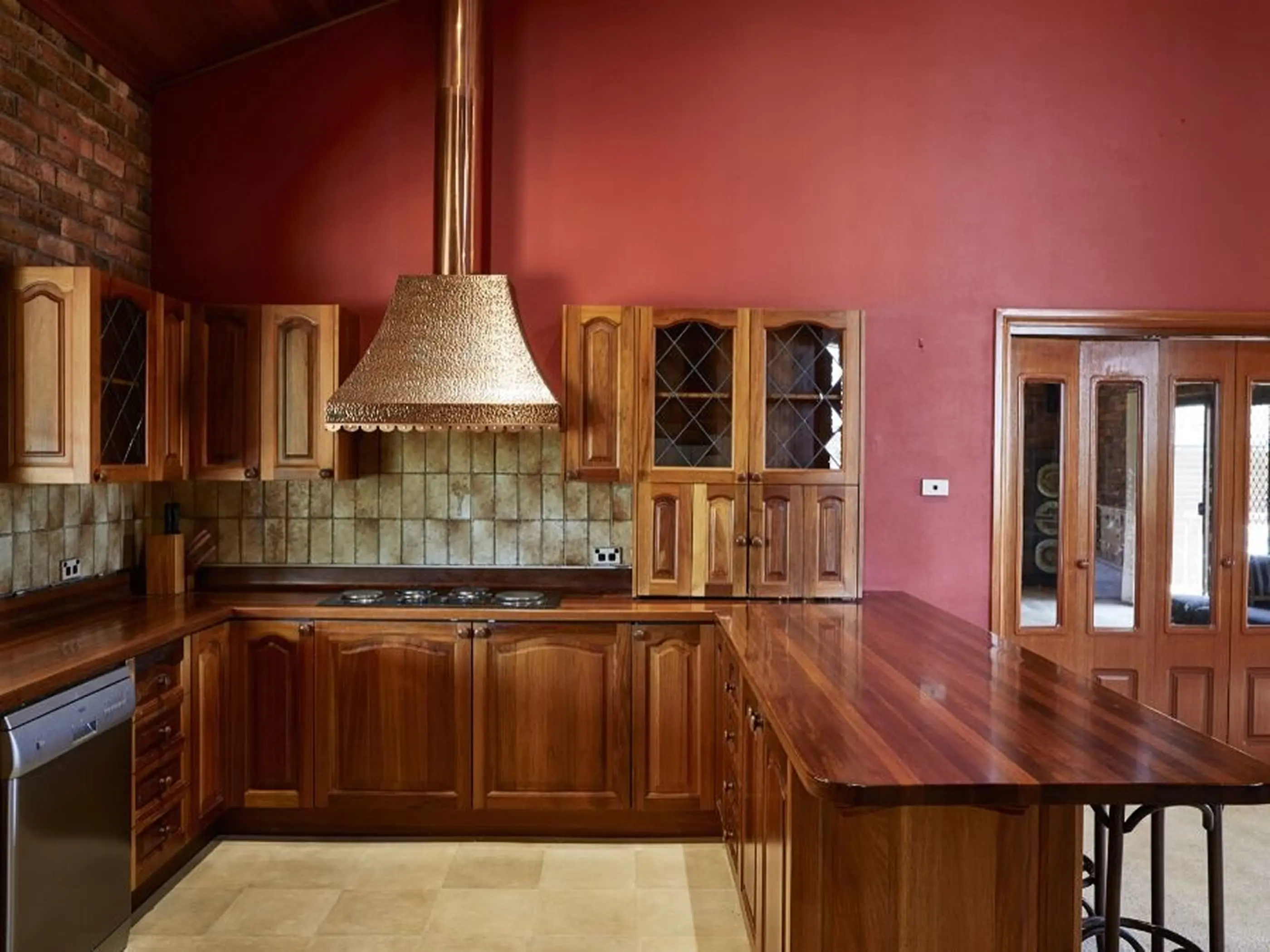Kitchen with wooden cabinets, polished countertop, and range hood against red walls with brick accent wall.
