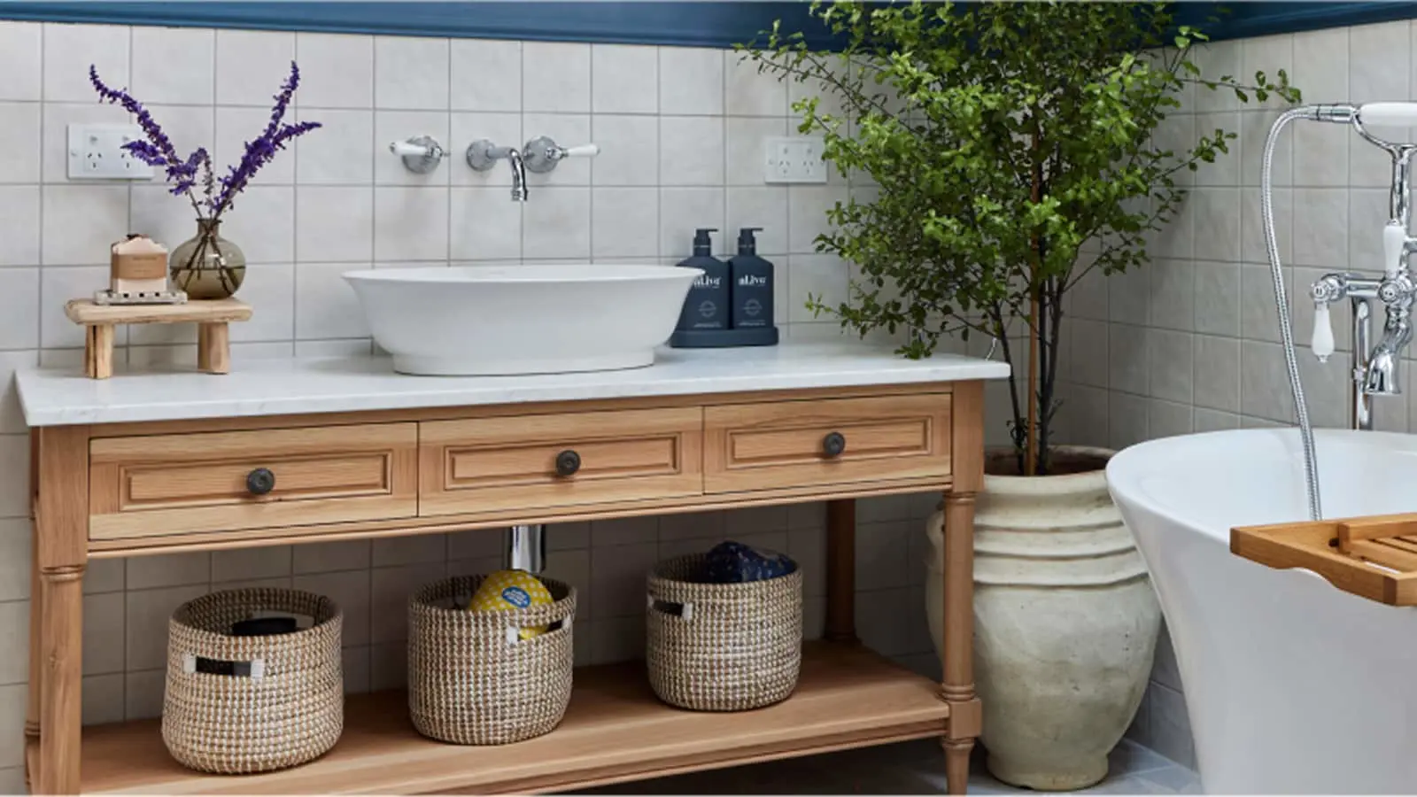 Modern bathroom with wooden vanity, white vessel sink, potted plant, woven baskets, and freestanding bathtub.