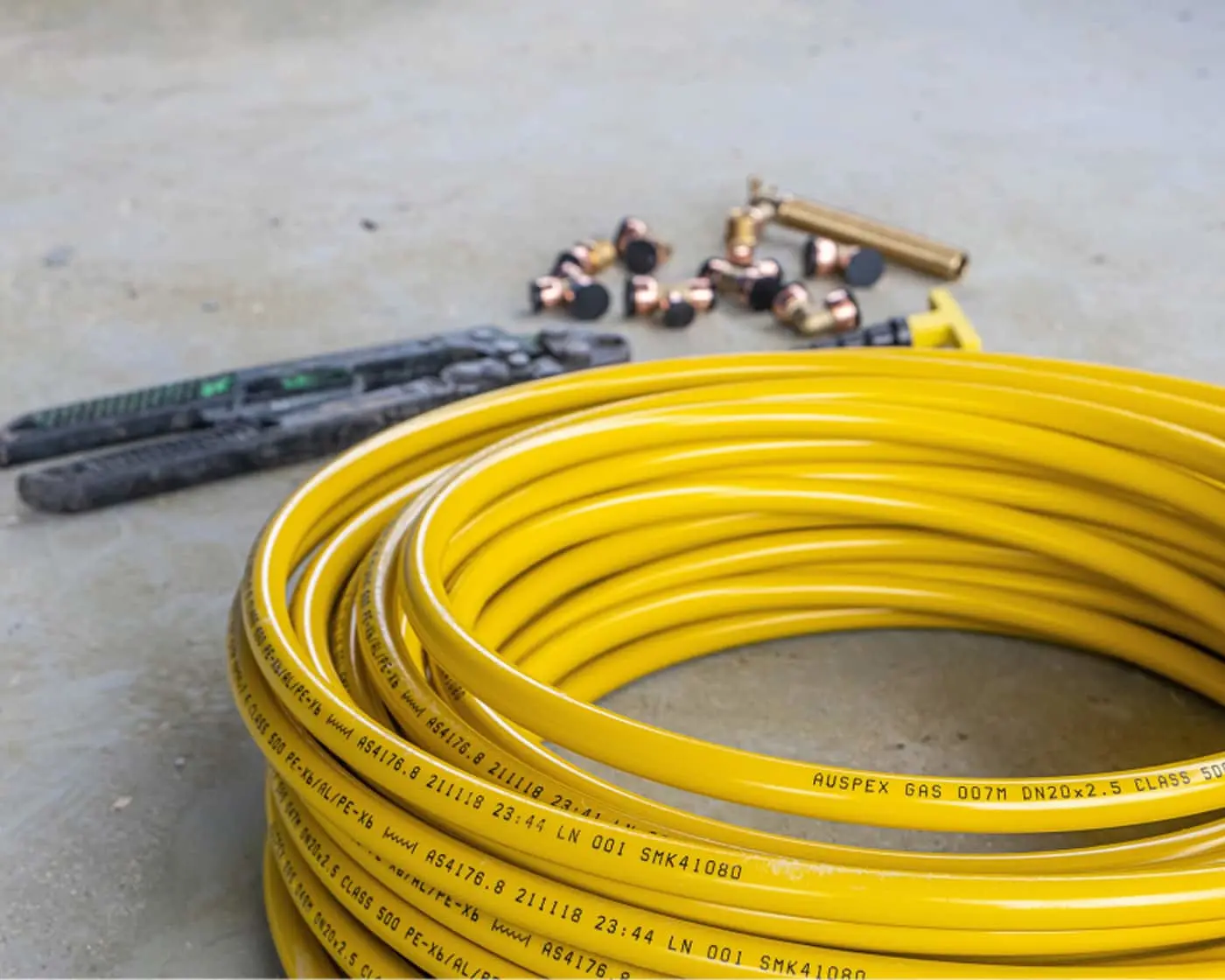 Coiled yellow gas pipe with brass fittings and plumbing tools on concrete floor.