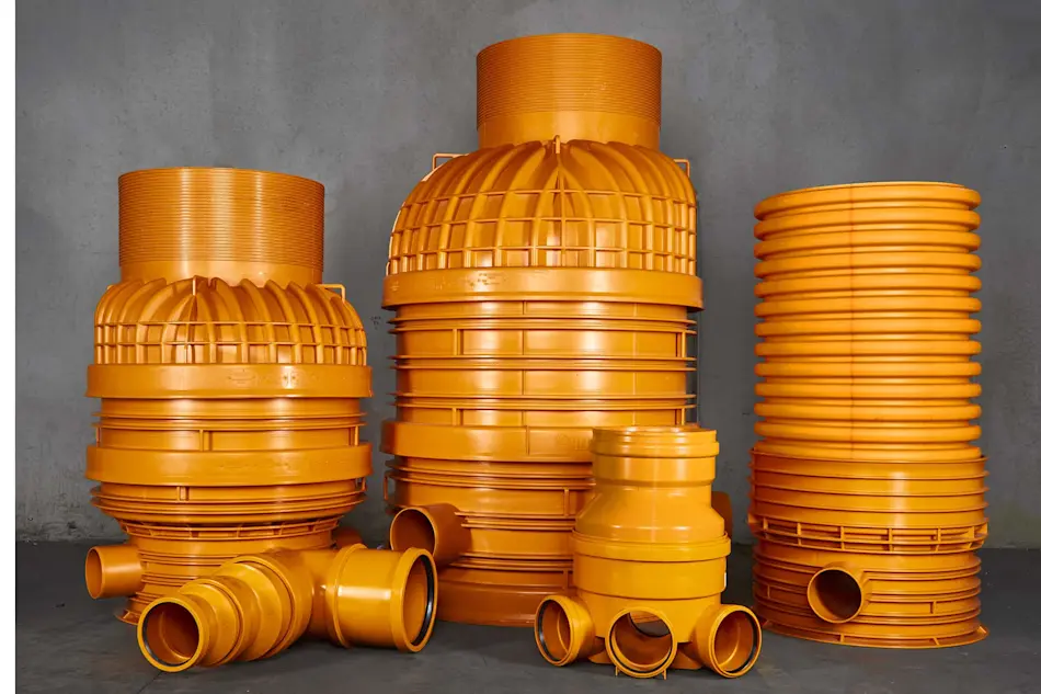 A collection of orange sewer system components with connecting pipes against a gray concrete wall.