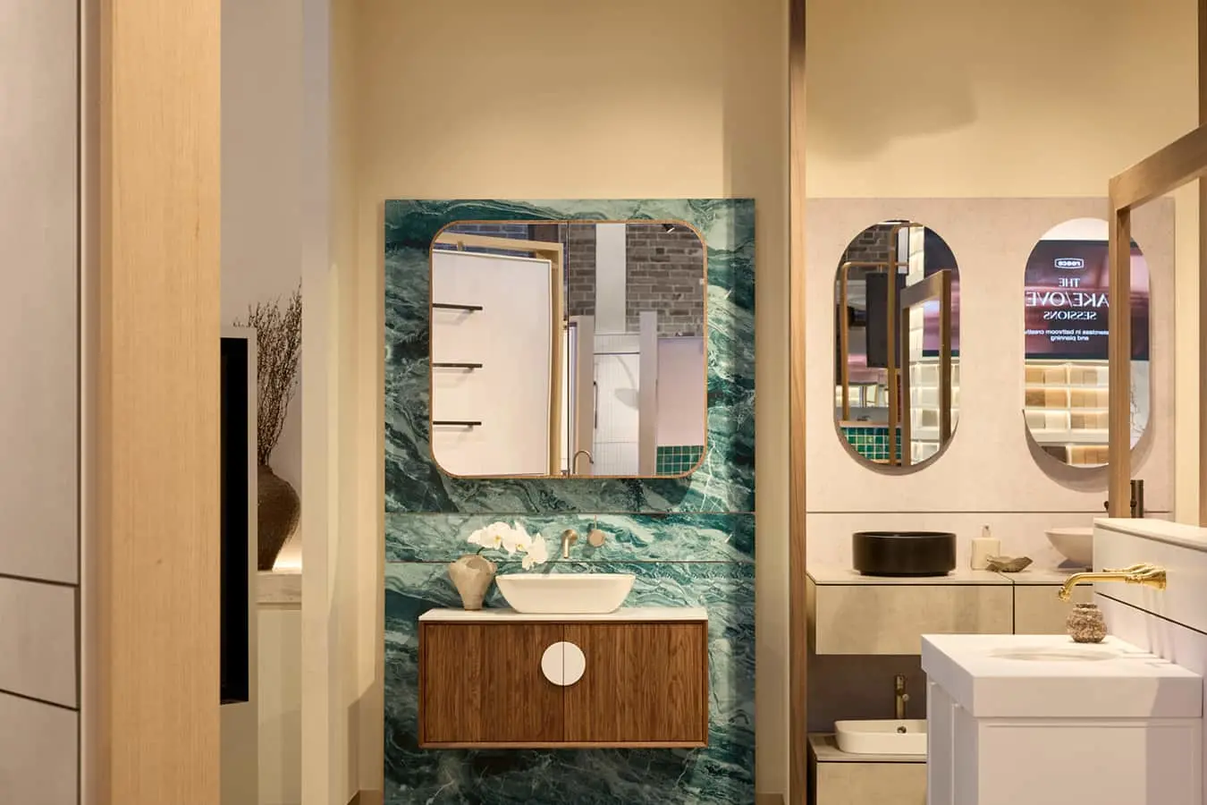 Bathroom display with green marble wall, wood vanity, white vessel sink, gold mirror, and orchid flowers.