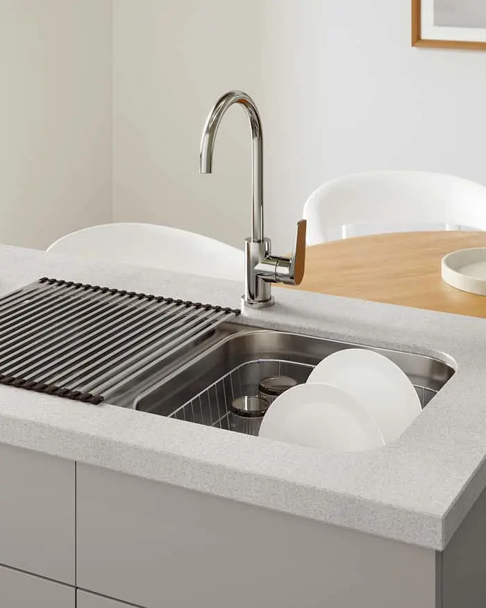 Chrome faucet over stainless steel sink with white plates and black drying rack on light countertop