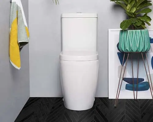 White one-piece toilet in a bathroom with dark herringbone floor, gray walls, yellow towel, and a teal geometric plant pot.