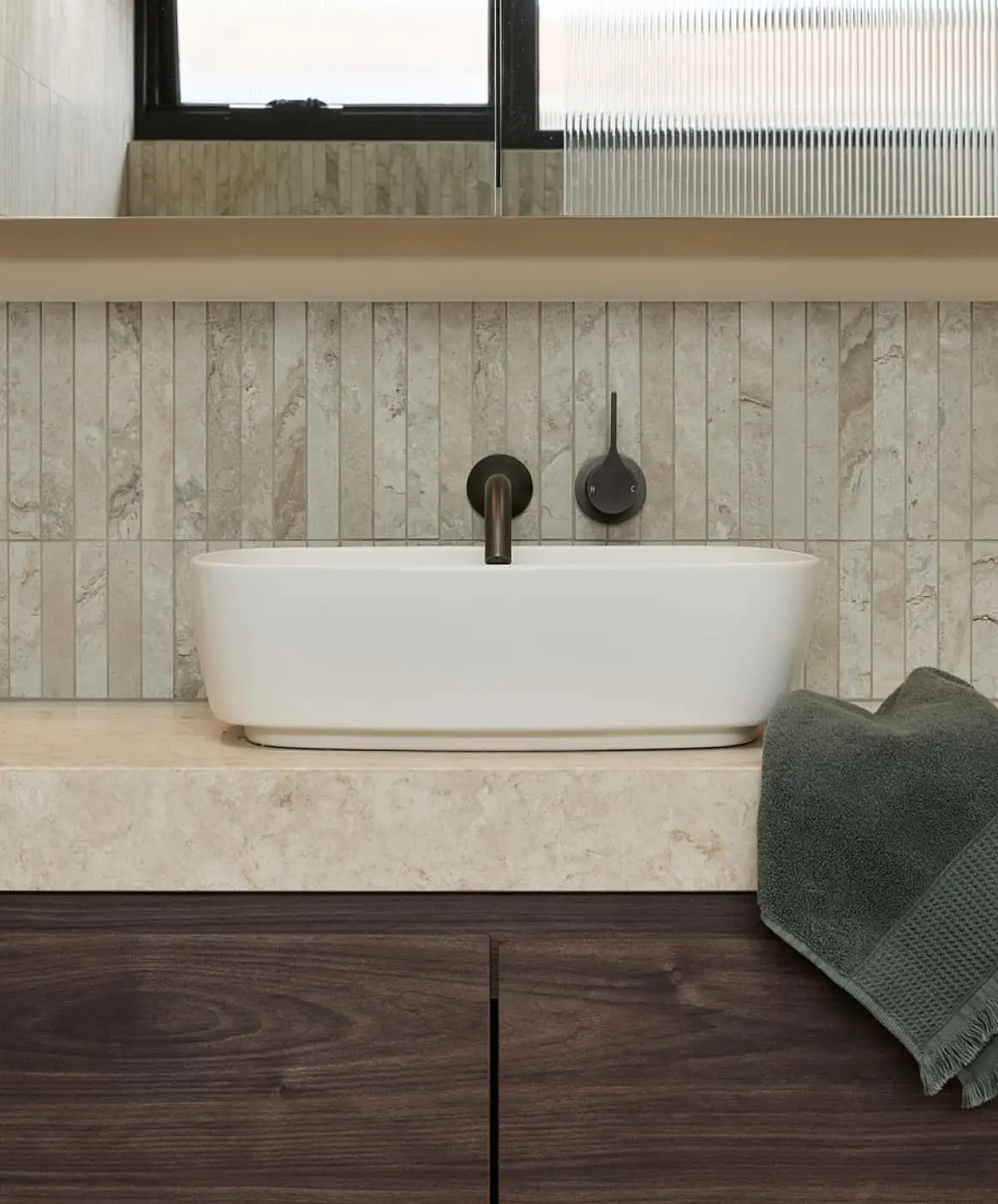 Modern bathroom with stone tile walls, dark wood vanity, white vessel sink, and minimalist fixtures. Gray towel on countertop.