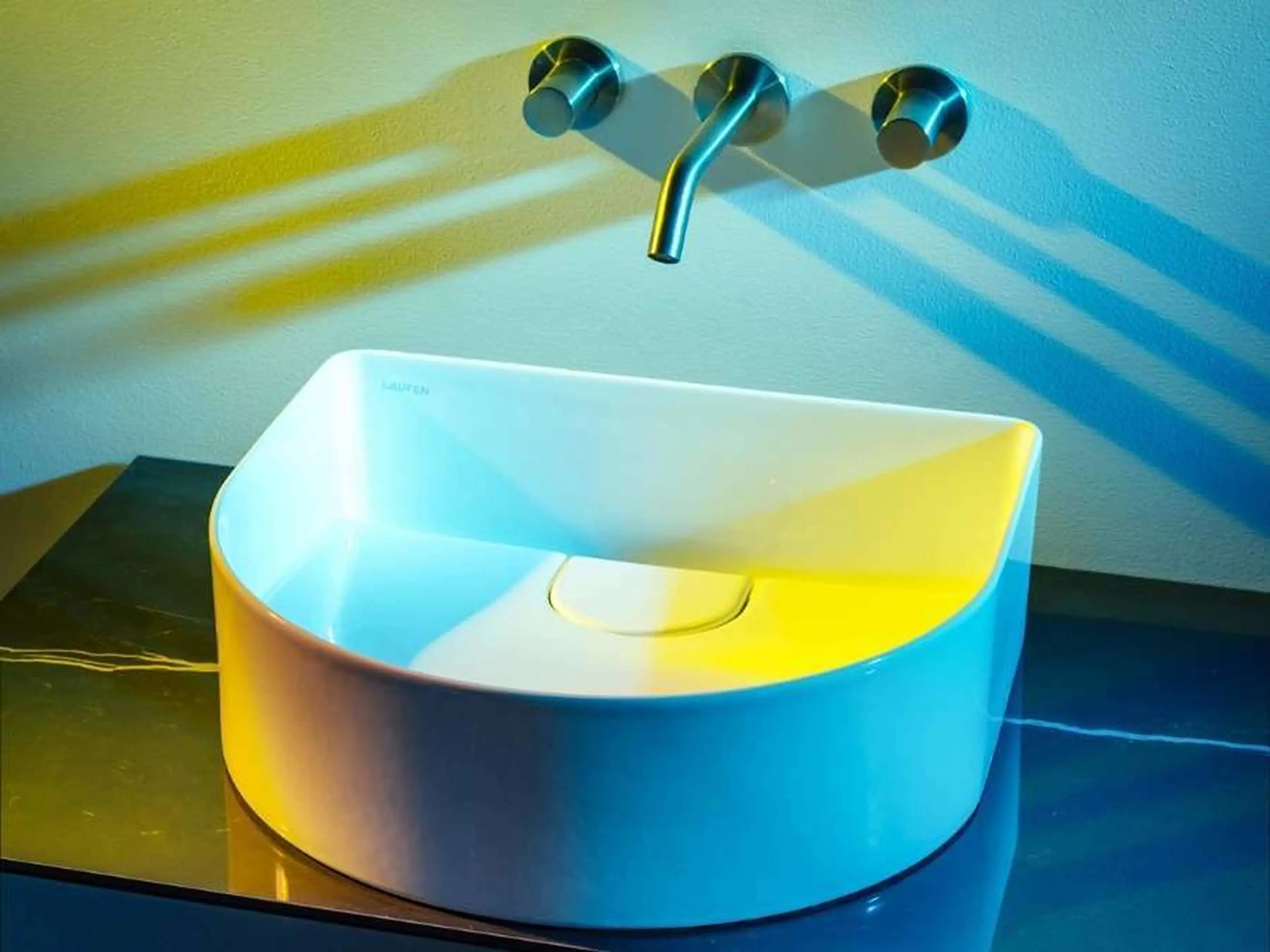 Modern white vessel sink with wall-mounted stainless steel faucet, illuminated by blue and yellow lighting.