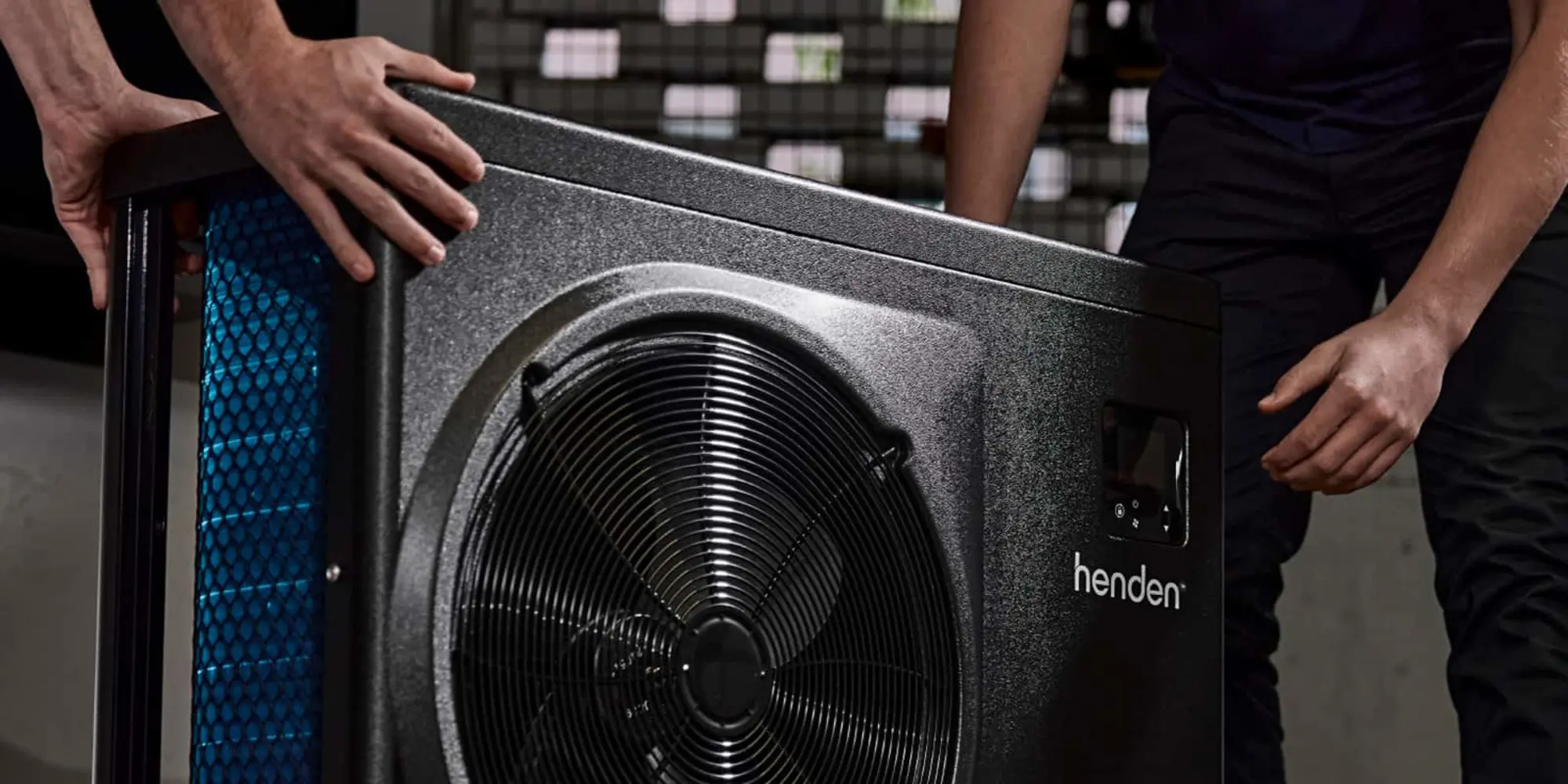 Hands installing a Henden heat pump unit with black fan grill and blue filter visible on the side.