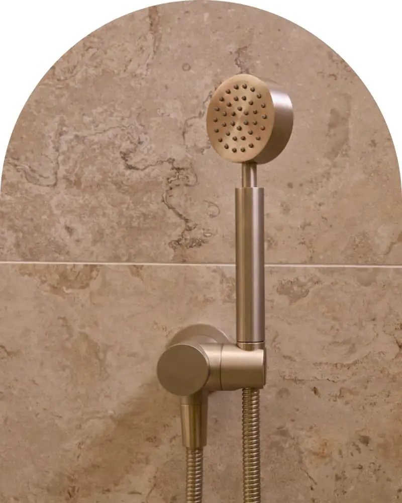 Brushed nickel handheld shower head with holder mounted on beige marble tile wall
