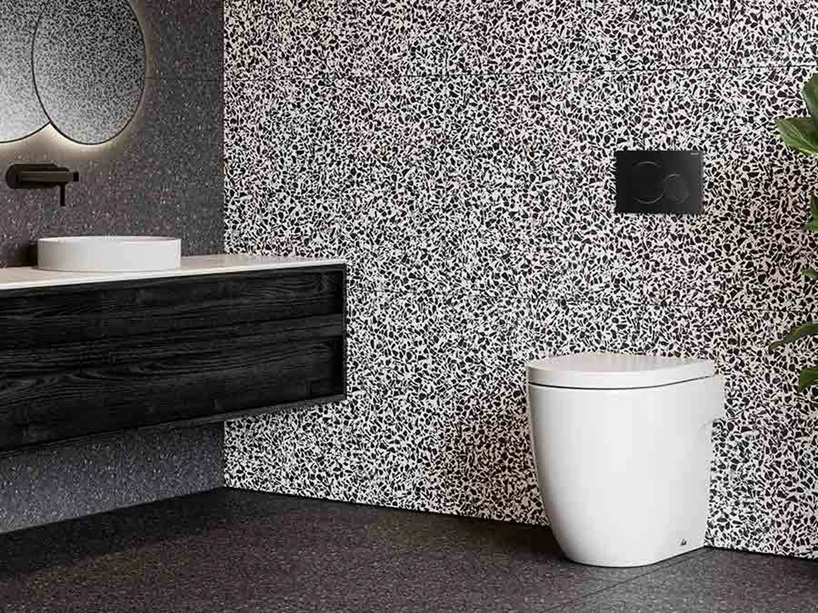 Modern bathroom with black and white speckled walls, dark wood vanity, white sink, and white toilet.