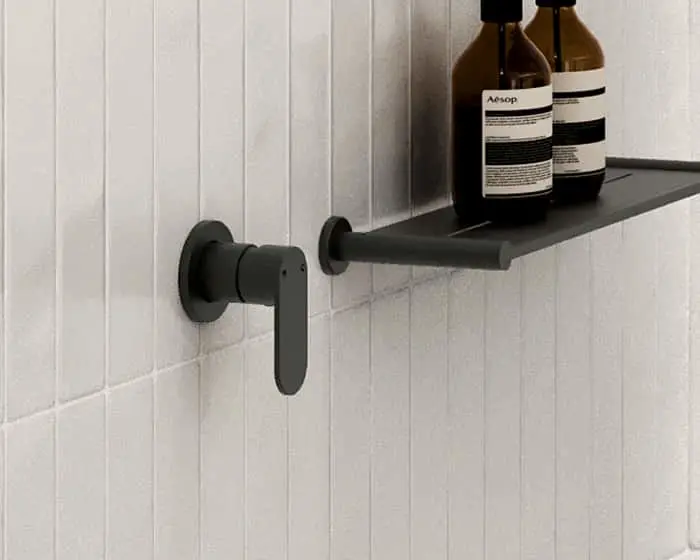 Two brown Aesop bottles on a black wall-mounted bathroom shelf with a modern black faucet against white tiled wall.