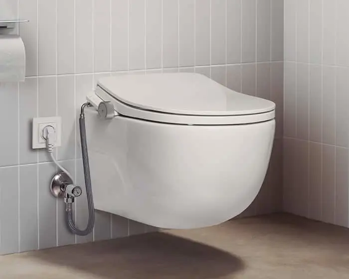 Modern wall-mounted white toilet with closed lid against light gray tiled wall, with water connection visible.