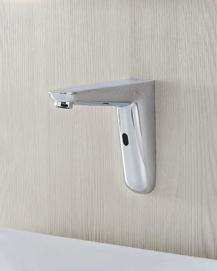 Modern chrome automatic sensor faucet mounted on a light beige textured wall above a white sink.