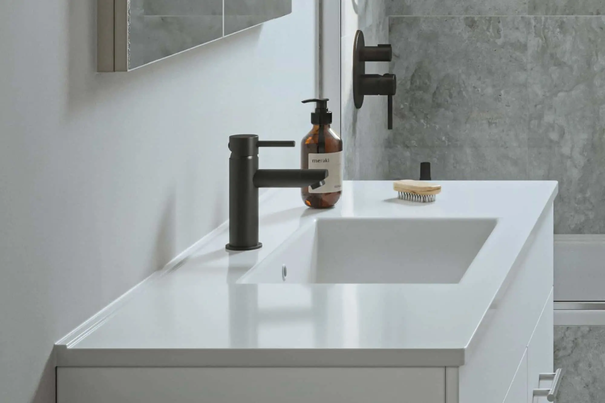 Modern bathroom sink with white countertop, black faucet, soap dispenser, and brush against gray tile wall.