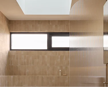 Modern bathroom interior with beige tiled walls, horizontal window, and wooden slatted partition feature.
