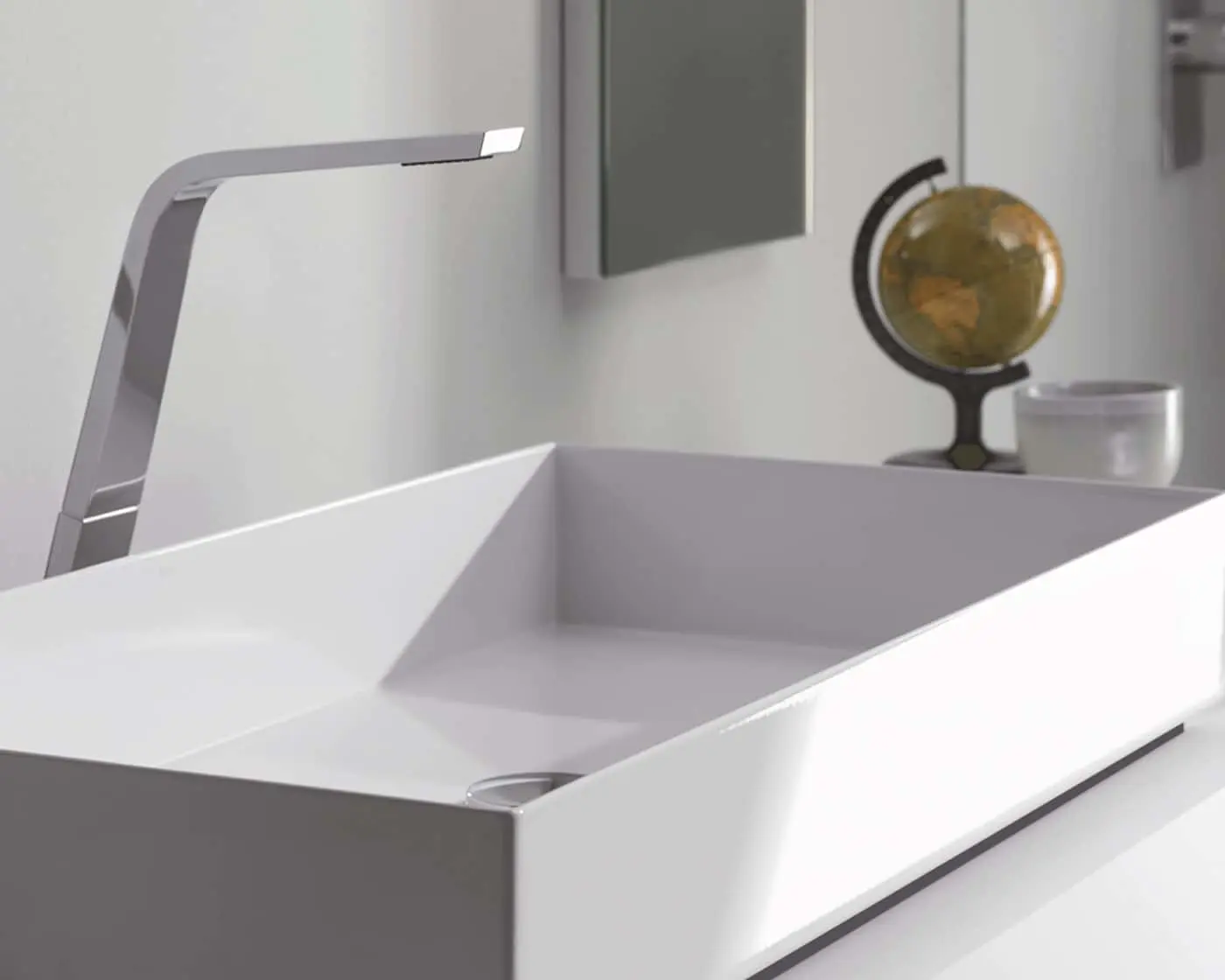 Modern white bathroom sink with chrome faucet, small decorative globe and white container on countertop.