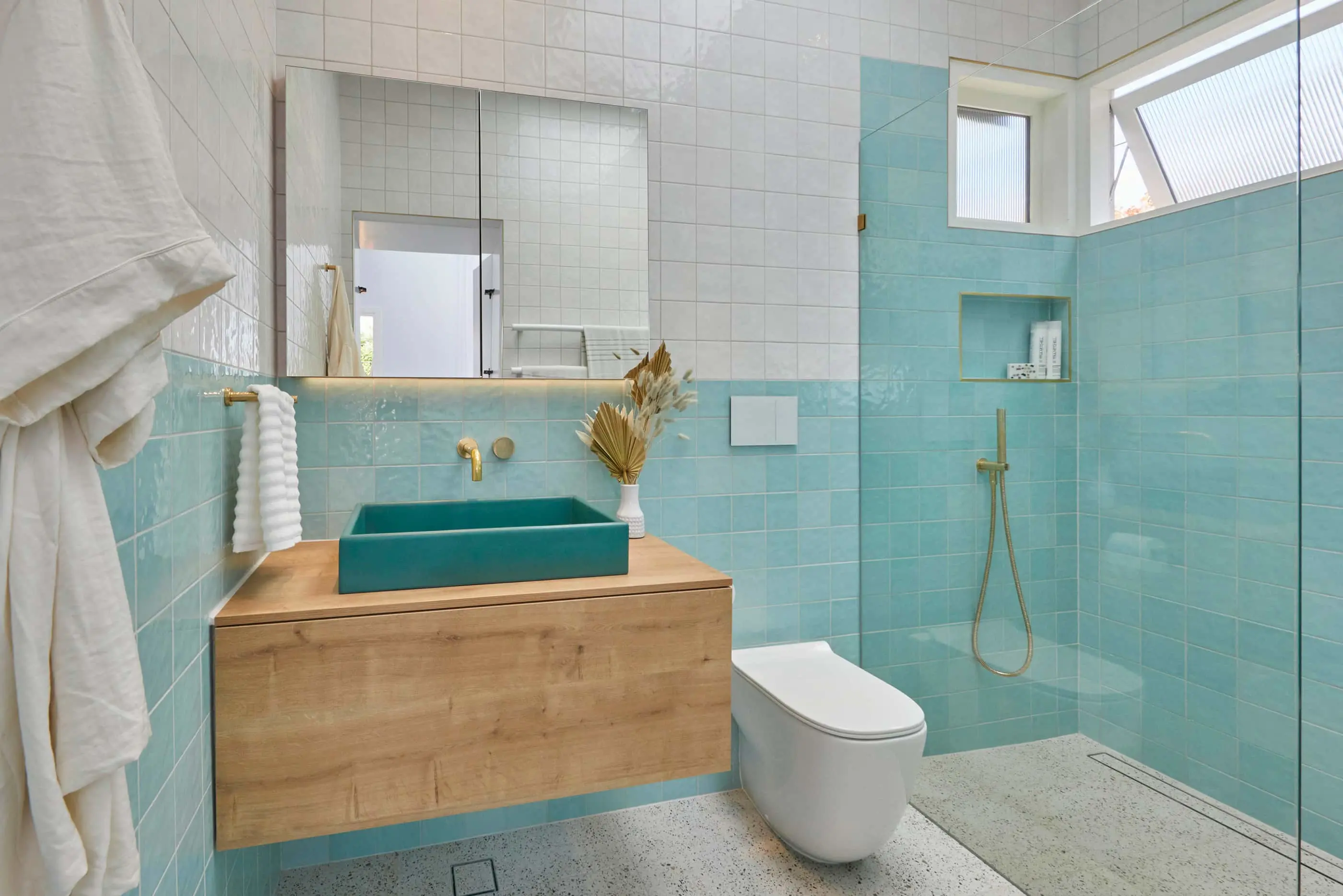 Modern bathroom with turquoise tiles, wooden vanity with matching sink, white toilet, and glass shower area.