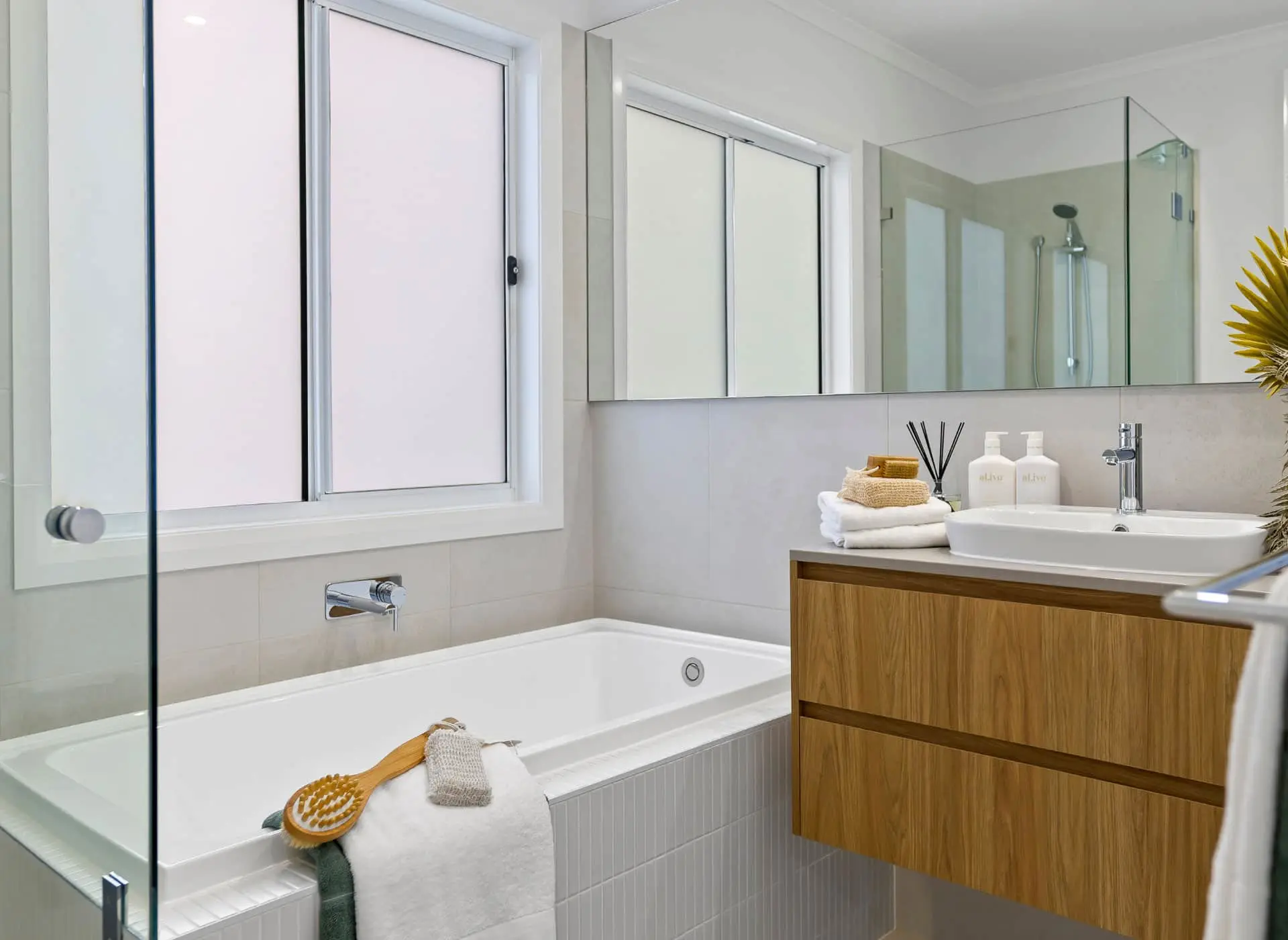 Modern white bathroom with bathtub, wooden vanity, glass shower partition, and frosted window.
