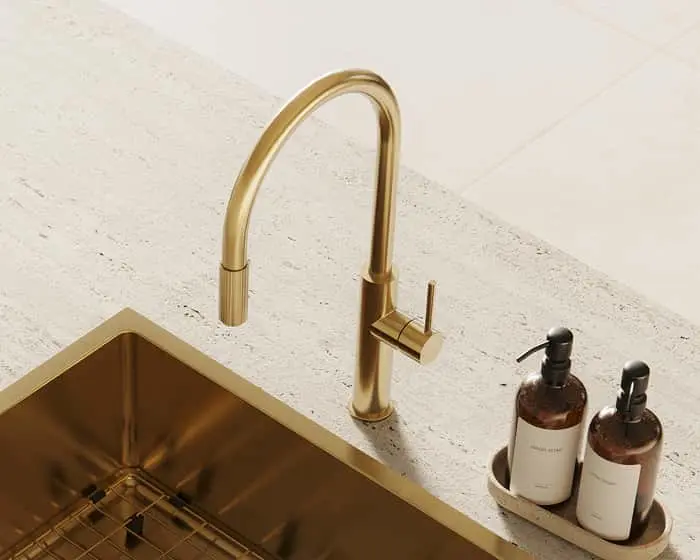 Brushed brass kitchen faucet with pull-down spout on a stone countertop beside a gold sink and two soap dispensers.