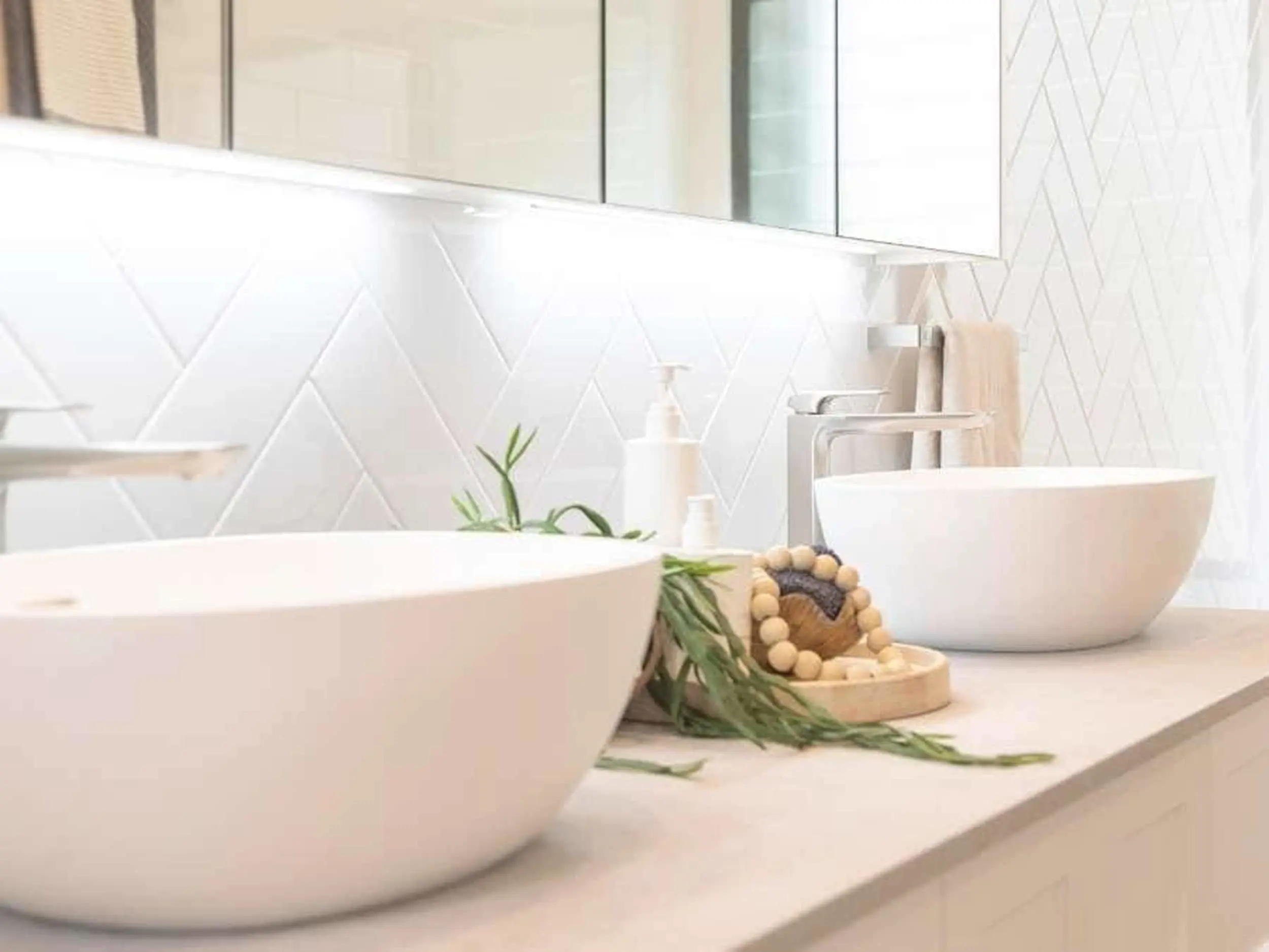 Modern bathroom with white vessel sinks, herringbone tile backsplash, and wooden bead decor on light countertop.