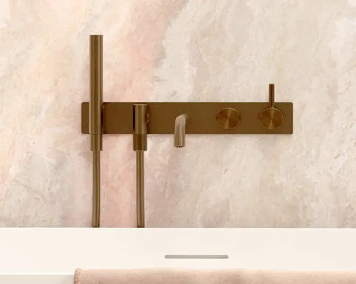 Modern bronze bathroom fixture with wall-mounted controls and shower components against a light marble wall.