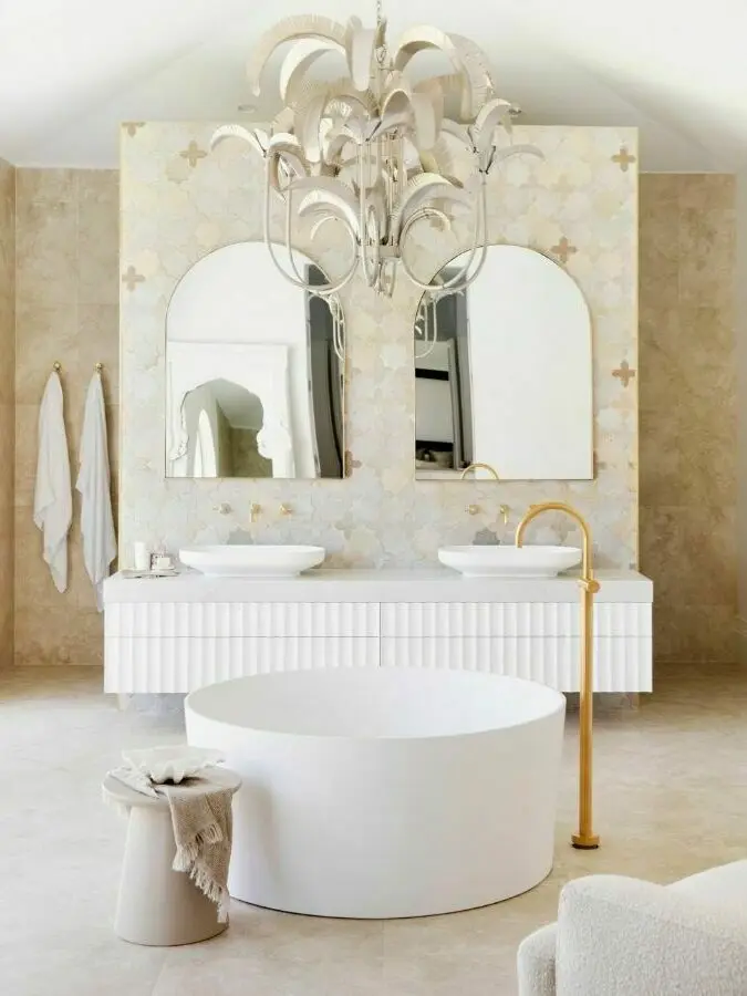 Elegant bathroom with white circular tub, white vanity with dual sinks, arched mirrors, and decorative chandelier.
