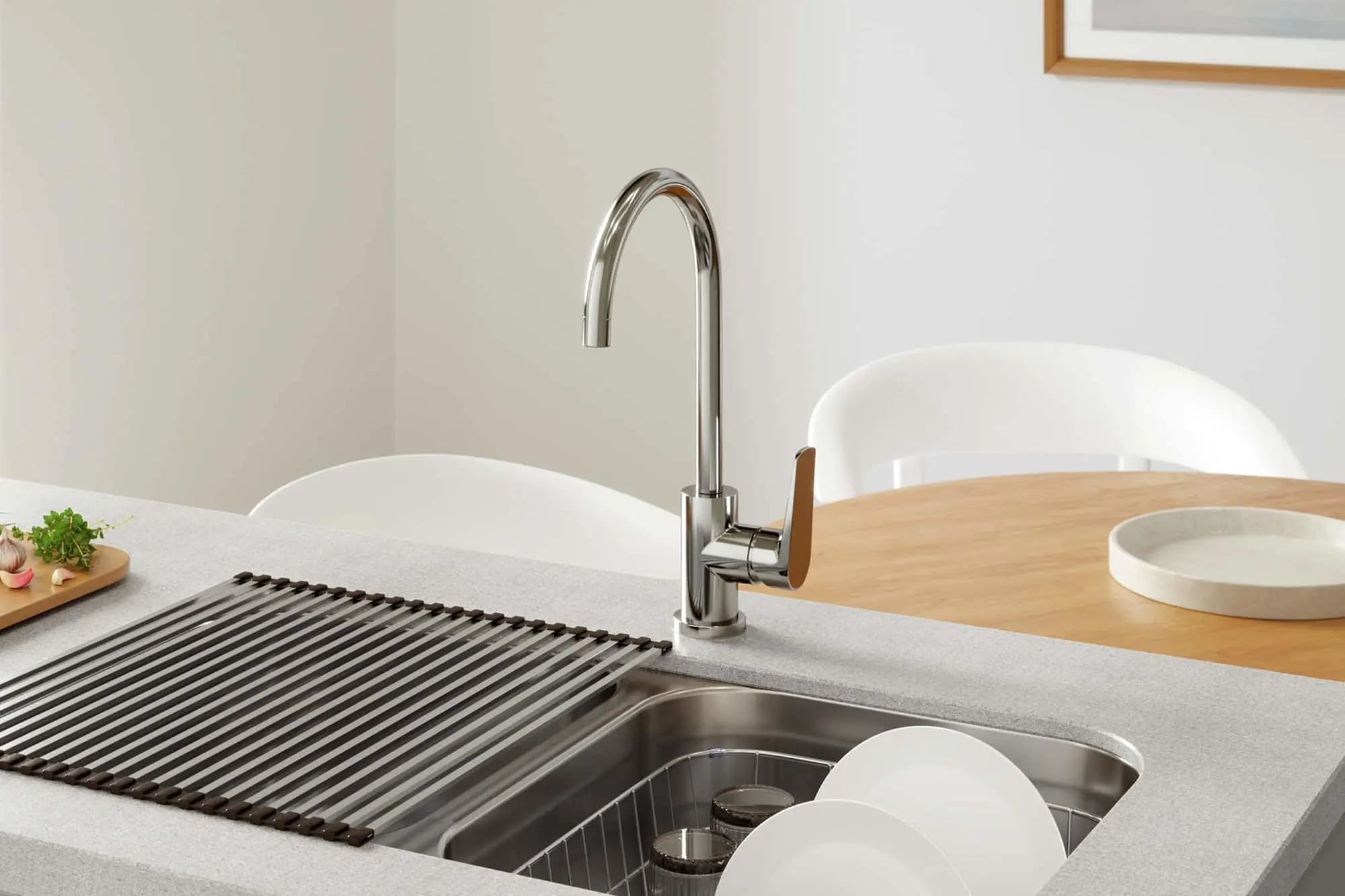Chrome kitchen faucet over stainless steel sink with white dishes and wooden cutting board on gray countertop.