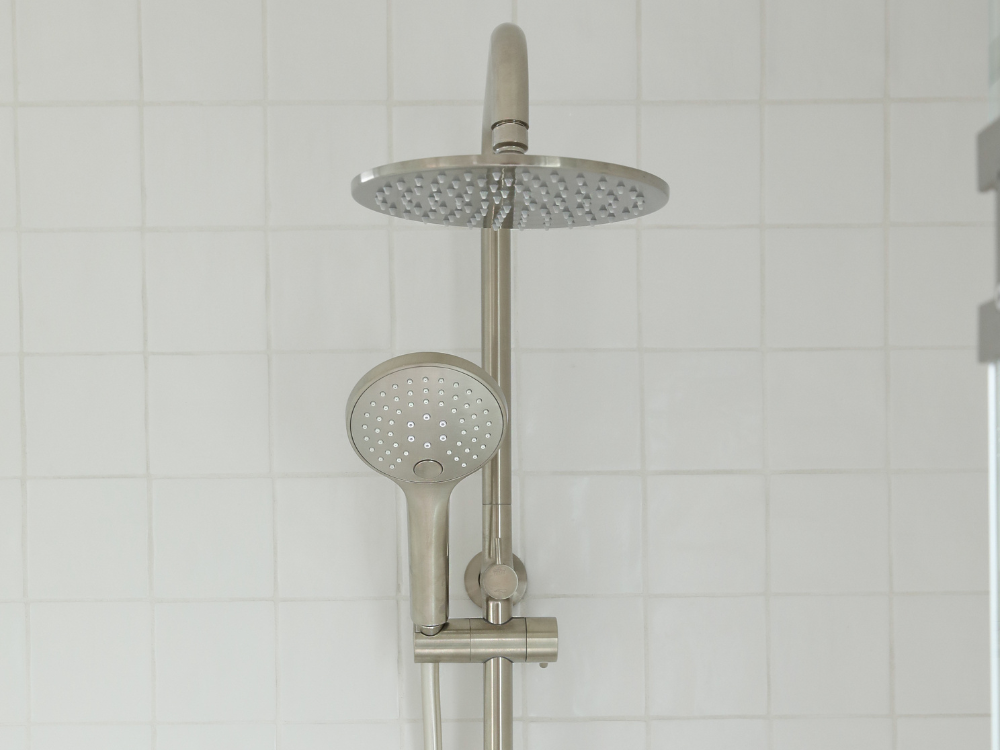 Modern stainless steel shower system with overhead rainfall showerhead and handheld sprayer against white tiled wall.