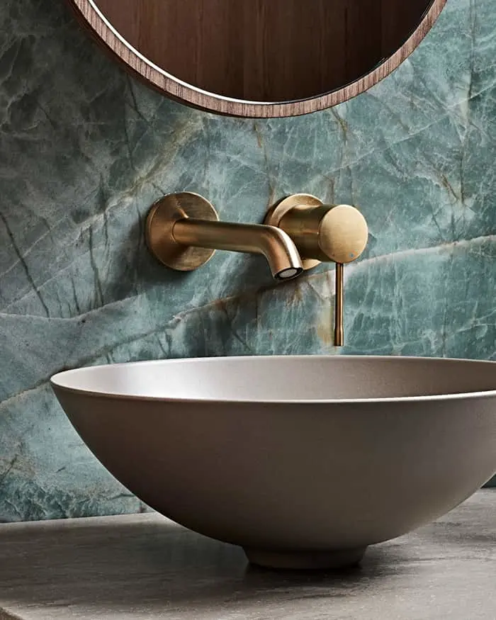 Modern bathroom with bowl sink, brass wall-mounted faucet, and green marble wall beneath circular mirror.