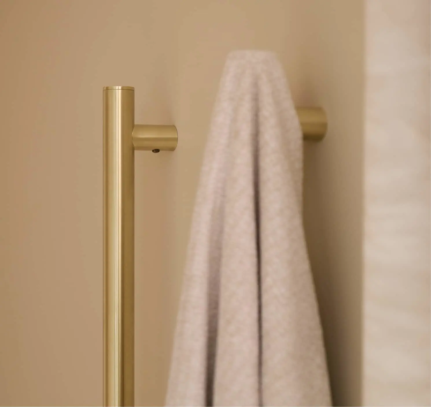 A brushed gold towel bar mounted on a beige wall, with a light grey towel draped over it.