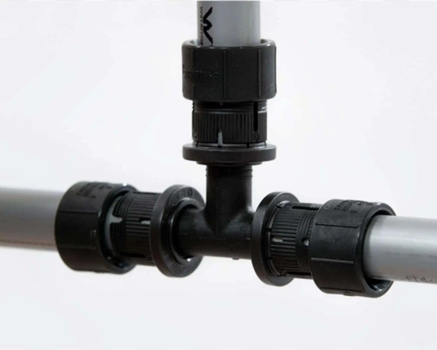 Black T-shaped pipe fitting connecting gray PVC pipes with compression connectors.