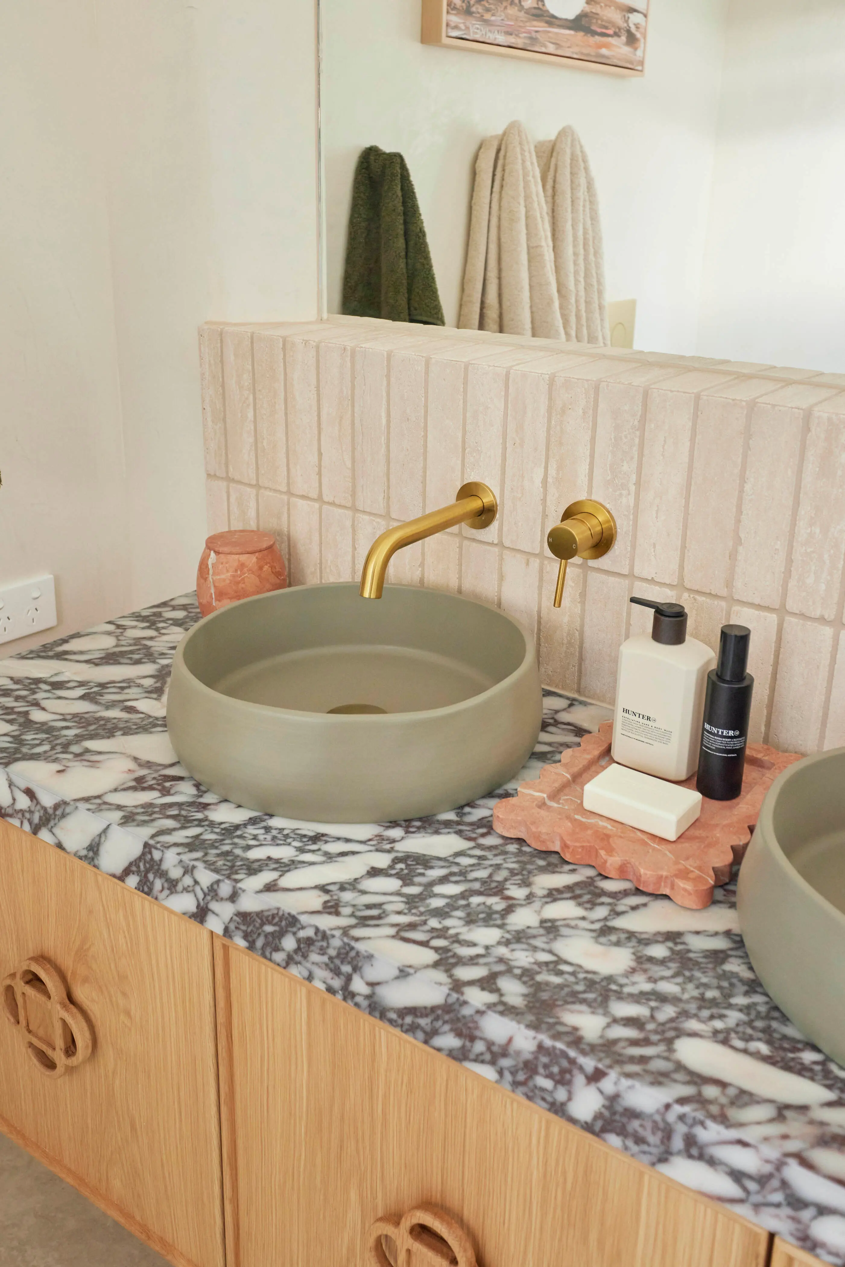 Modern bathroom with green vessel sink, brass faucet, marble countertop, and toiletries on terracotta tray.