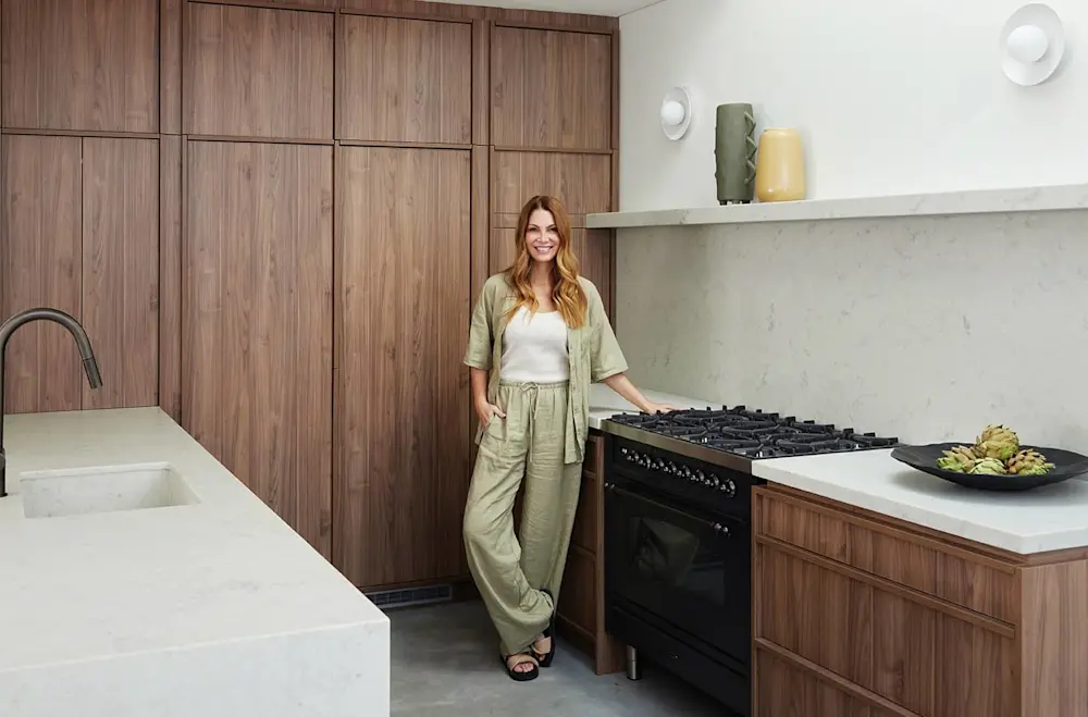 Person in green outfit standing in modern kitchen with wooden cabinets, gas stove, and marble countertops.