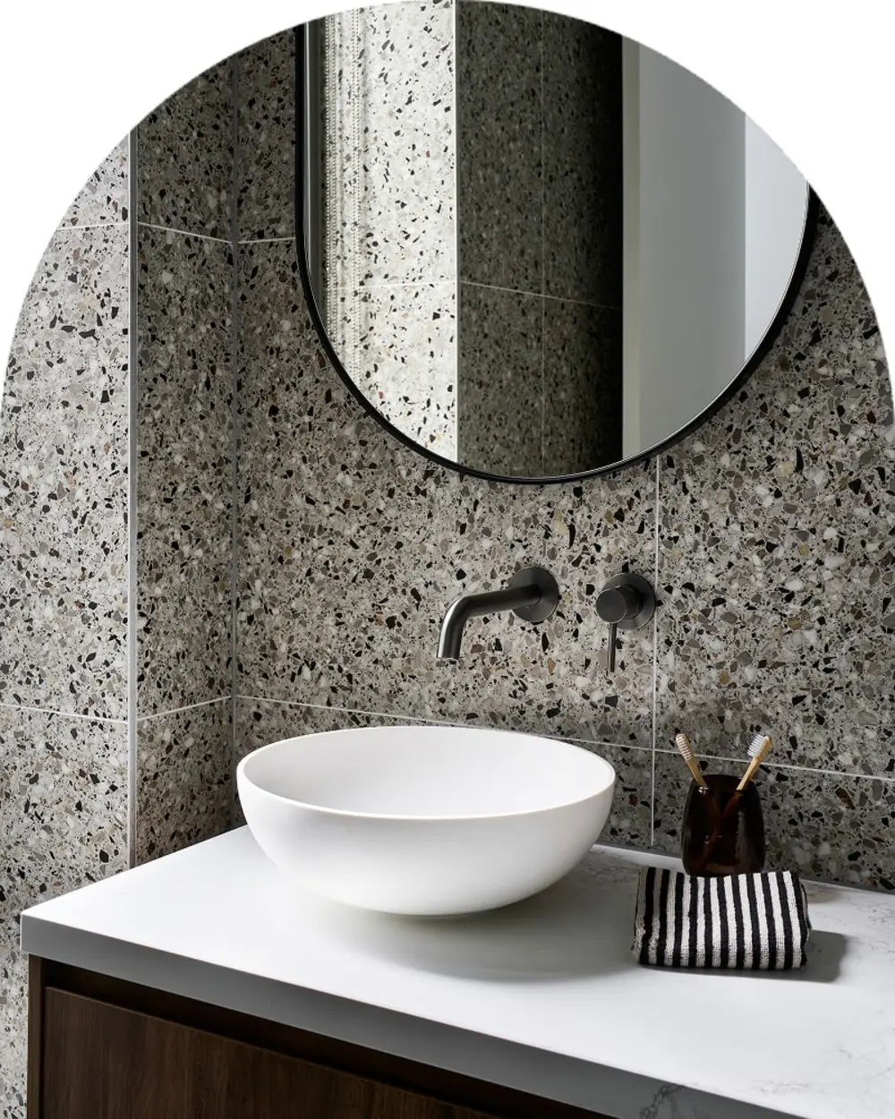 Modern bathroom with terrazzo tile walls, white vessel sink, round mirror, and wall-mounted faucet.