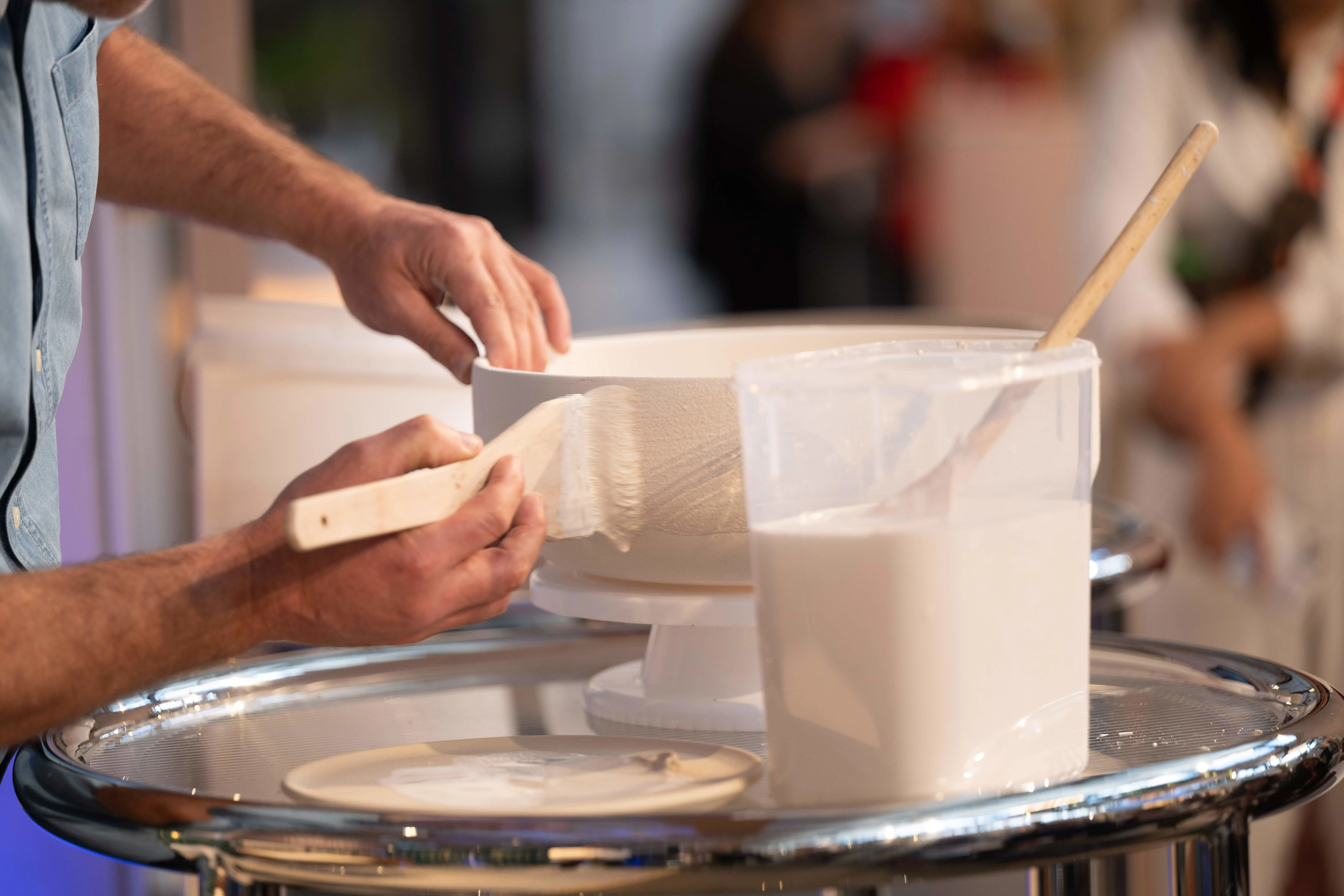 Person applying a glaze to a white basin with a brush on a rotating stand.
