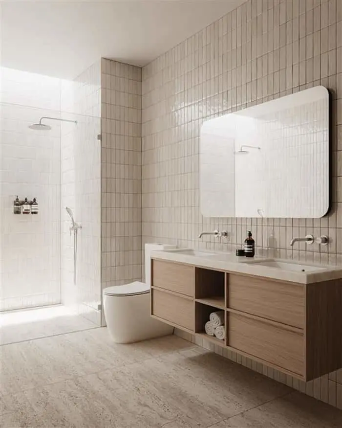 Modern bathroom with beige tile walls, floating wooden vanity with double sinks, white toilet, and glass shower enclosure.