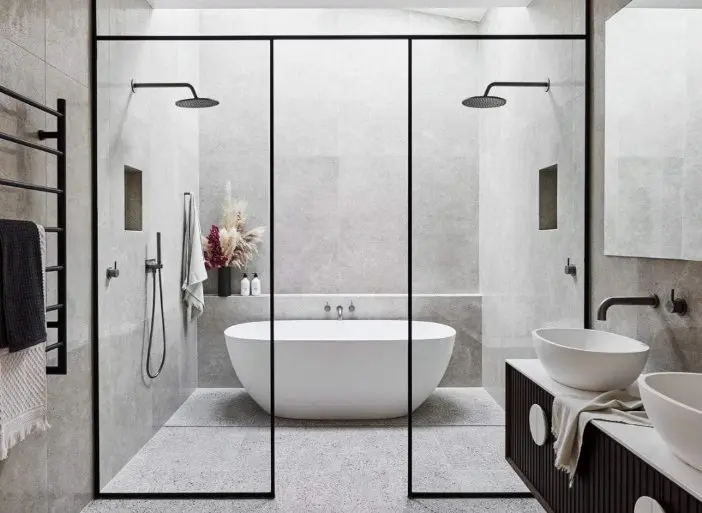 Modern bathroom with white freestanding tub, glass shower enclosure, dual rainfall showerheads, and twin vessel sinks on dark vanity.