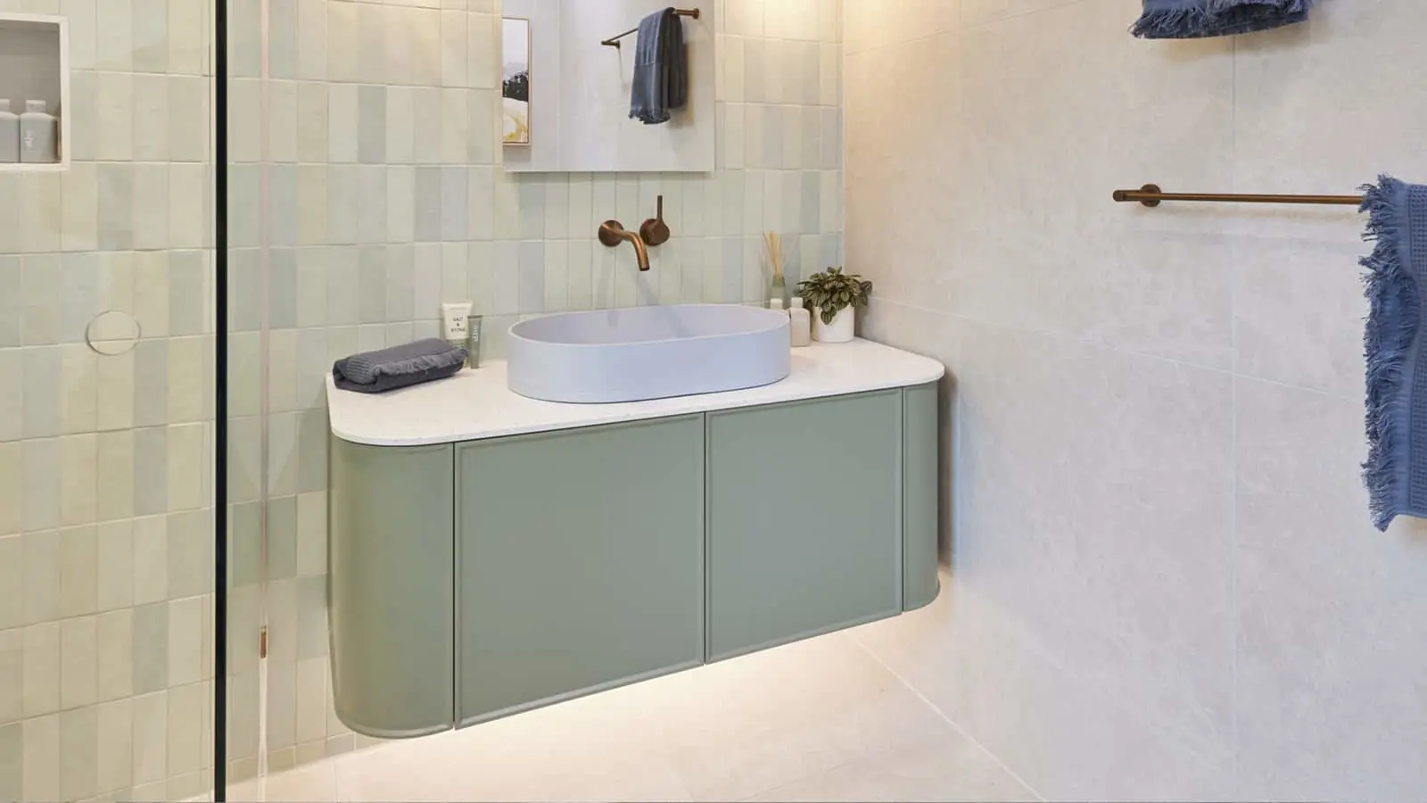 Modern bathroom with mint green vanity, oval sink, brass fixtures, and blue towels on wall-mounted racks.